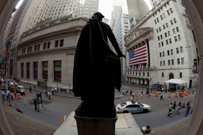 Di belakang bendera besar AS yang menutupi barisan tiang, fasad Bursa Efek New York diawasi oleh patung George Washington di Wall Street.