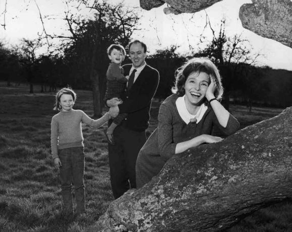 Foto hitam putih Roald Dahl menggendong anak-anaknya; istrinya Patricia Neal bersandar di pohon