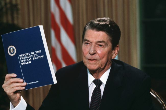 Presiden Ronald Reagan memegang salinan laporan Komisi Menara tentang skandal Iran-Contra