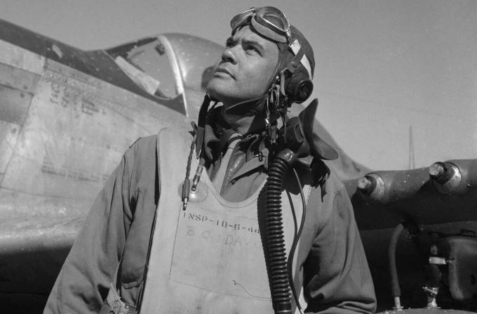 Benjamin O. Davis dengan jas terbang dan helm berdiri di depan pesawat tempur P-51 Mustang.