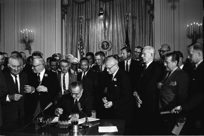 Presiden Lyndon B. Johnson menandatangani Undang-Undang Hak Sipil 1964 saat Martin Luther King, Jr., dan lainnya, menonton.