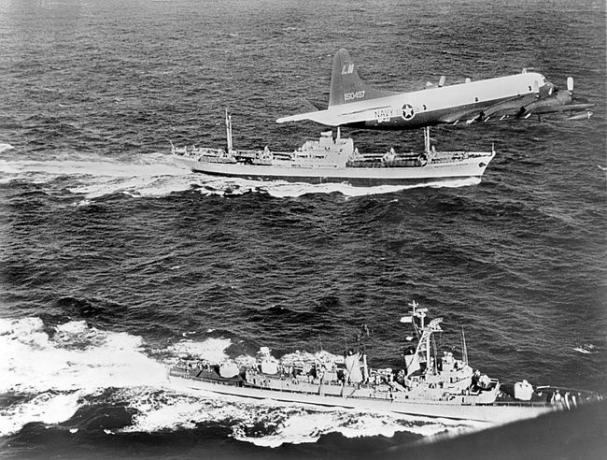 Kapal barang Soviet Anosov, belakang, dikawal oleh pesawat Angkatan Laut dan kapal perusak USS Barry, saat meninggalkan Kuba selama Krisis Rudal Kuba 1962.