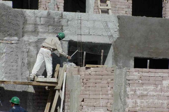 pria bertopi keras di perancah bekerja di dinding blok bumi